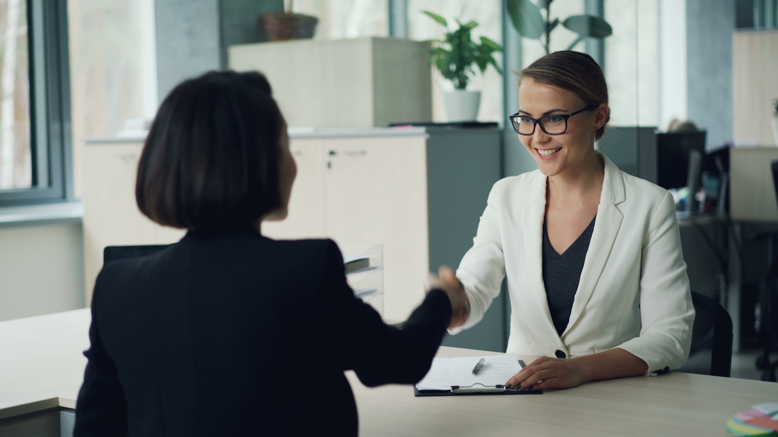 Two people shaking hands across a desk after reviewing paperwork